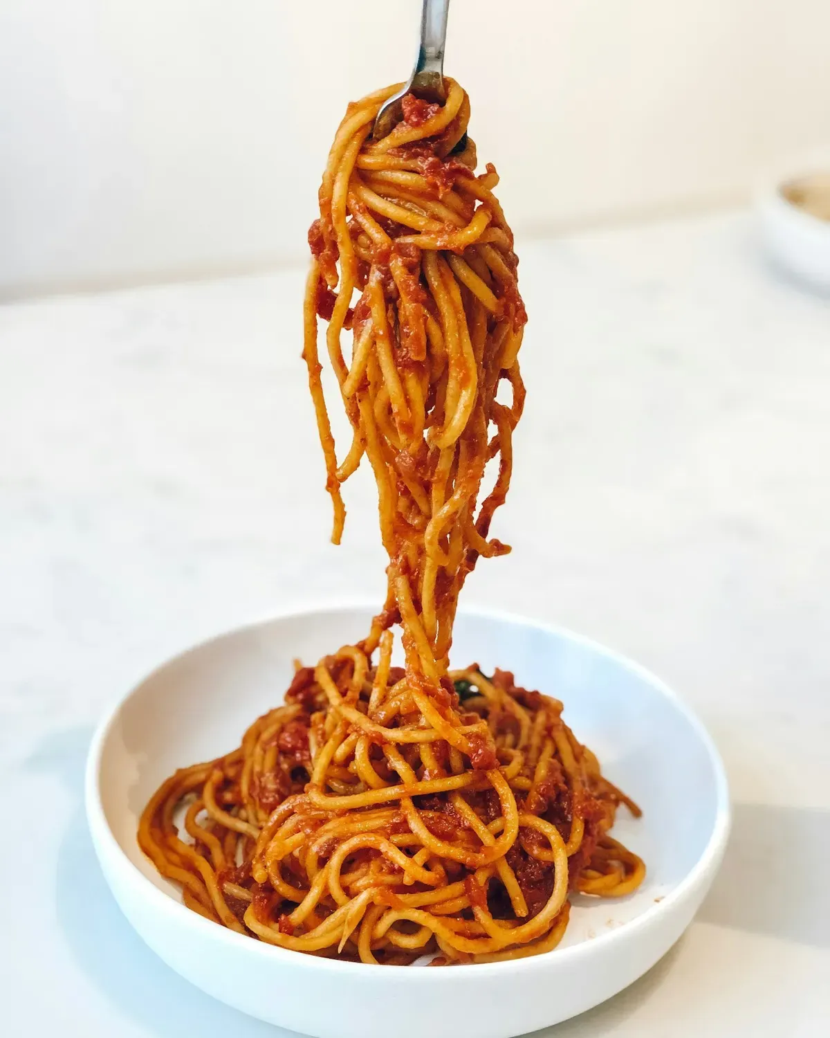 Macarrão espaguete com molho de tomate erguido com garfo sobre tigela branca